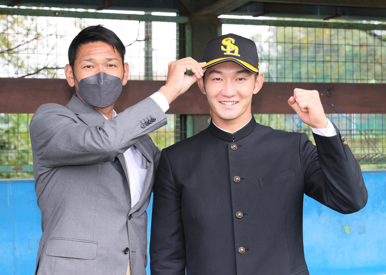 ソフトバンクドラフト2位の慶大・正木（右）は指名あいさつを受け、永井編成育成本部長兼スカウト部長から帽子をかぶせてもらい笑顔（撮影・足立雅史）