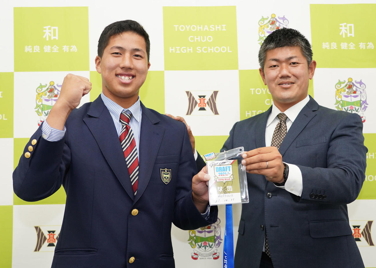 清水スカウト（右）から与田監督のサイン入りドラフト2021パスを受け取る中日ドラフト5位の星野真生（左）（撮影・森本幸一）