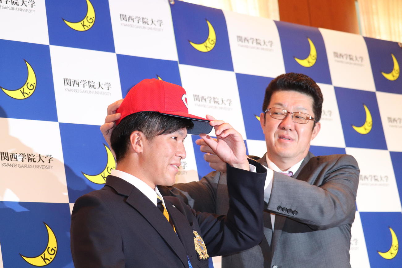 広島佐々岡真司監督から指名あいさつを受け、カープ帽子をかぶせてもらうドラフト1位関学大・黒原拓未投手（撮影・前原淳）