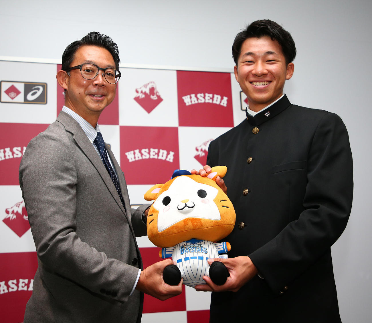 DeNA指名あいさつ　DeNAの八馬スカウト（左）からマスコット人形を受け取るドラフト2位の早大・徳山壮磨（代表撮影）