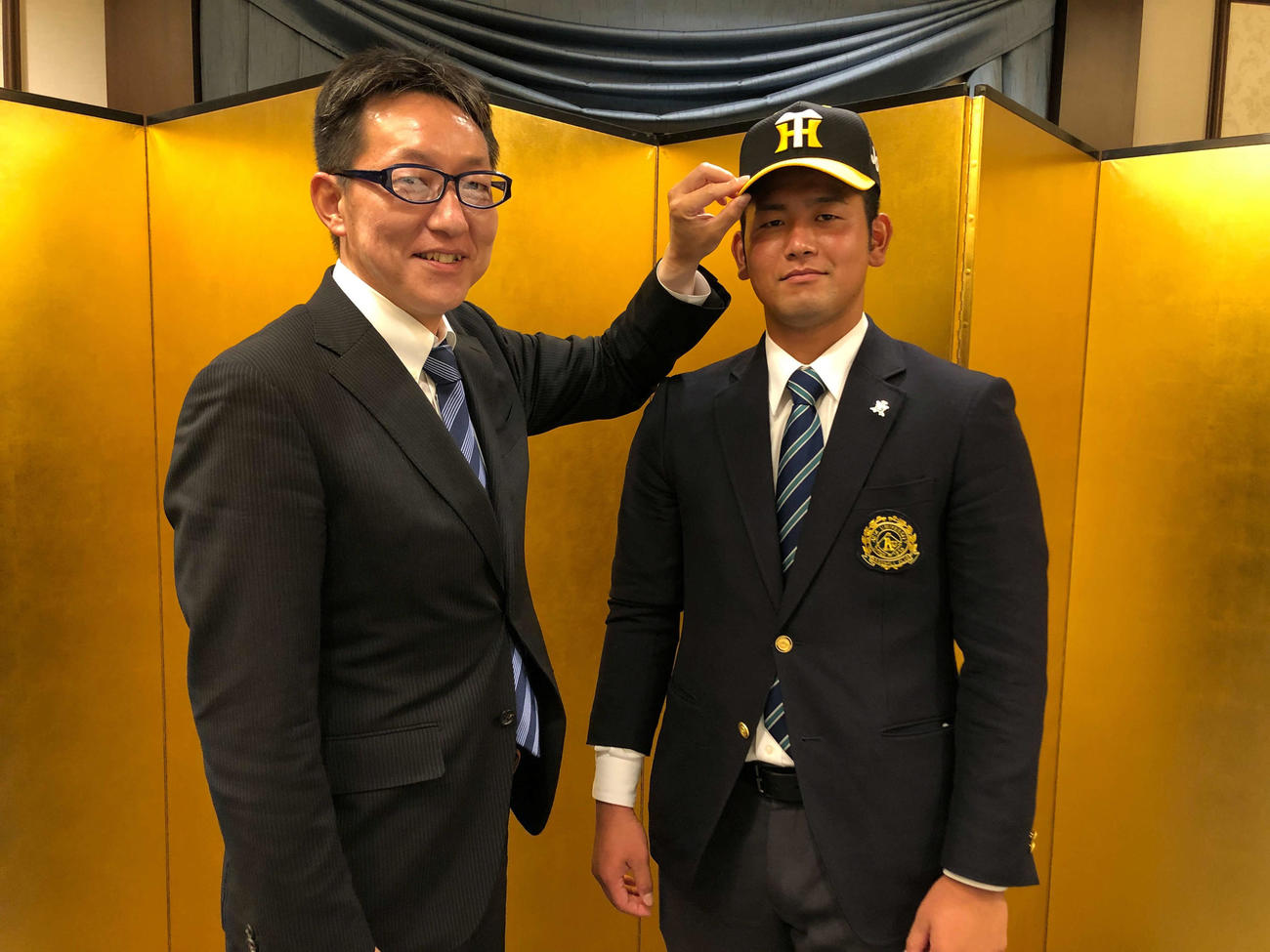 阪神と仮契約を結んだ岡留（右）は吉野スカウトに帽子をかぶせてもらう（球団提供）