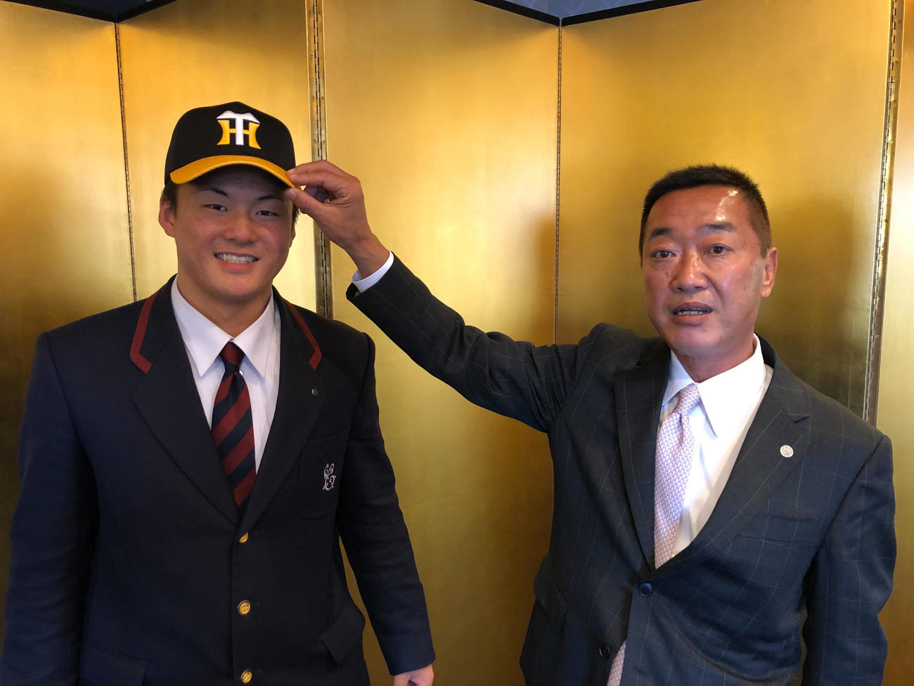 仮契約を結び、山本スカウト（右）から帽子をかぶせてもらう阪神ドラフト4位の前川右京（球団提供）