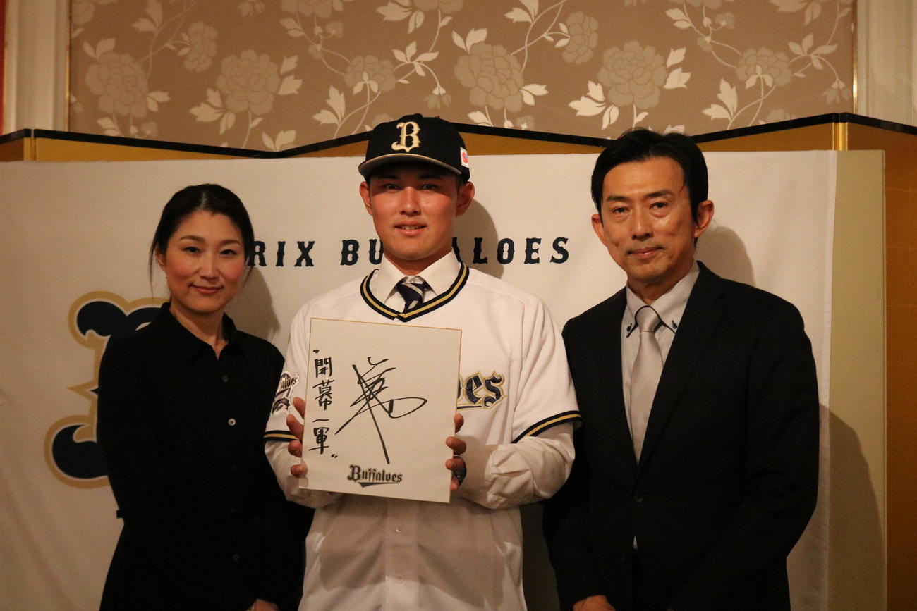 野口智哉内野手（22＝関大）は「開幕一軍」と書いた色紙を手に、父肇さんと母佳奈子さんと写真に納まる（撮影・林亮佑）