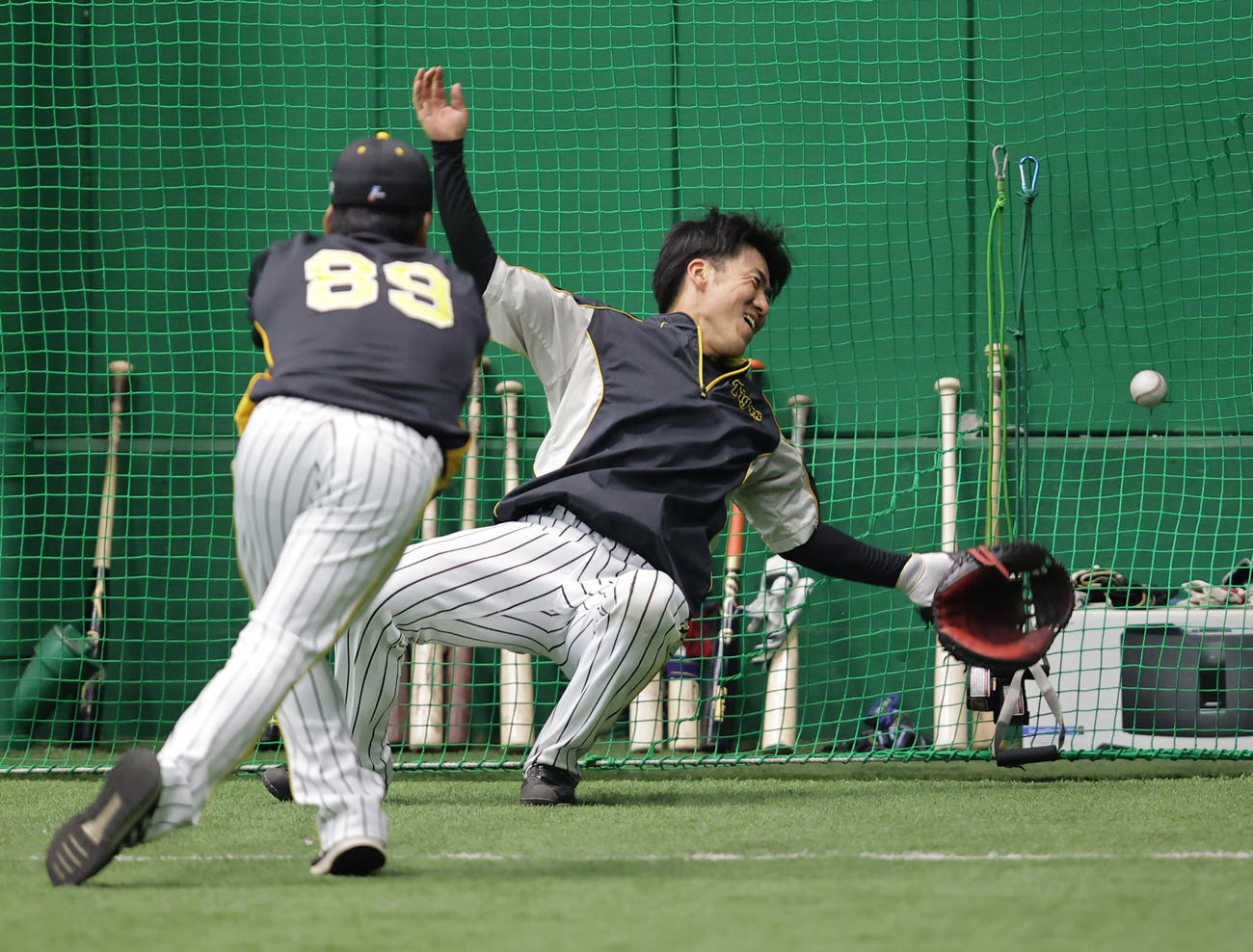 両手にボールを持つ藤井彰コーチ（手前）から放たれたボールに反応し飛びつく長坂（撮影・清水貴仁）