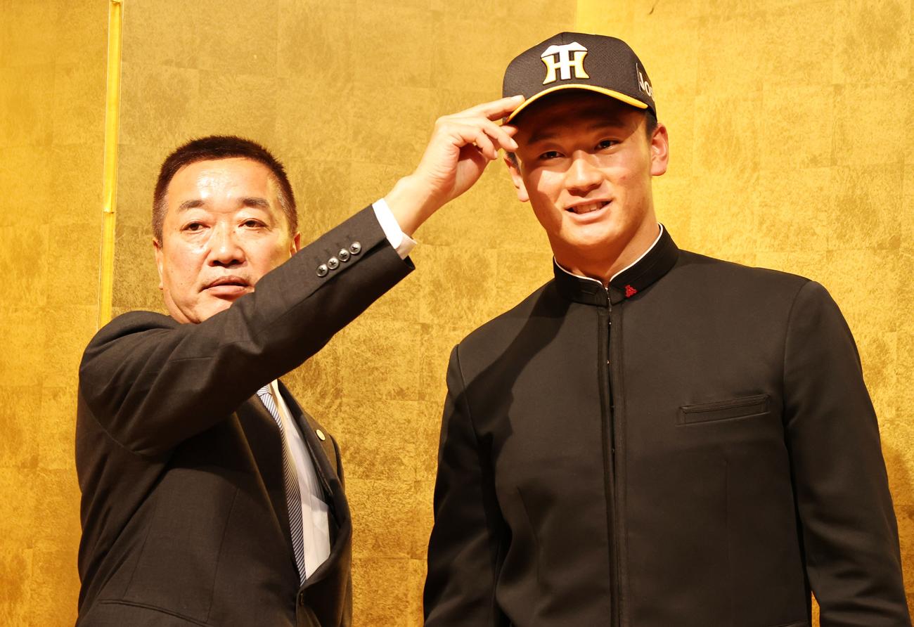 仮契約を終え山本スカウト（左）から帽子をかぶせてもらう阪神ドラフト１位指名の森木（撮影・加藤哉