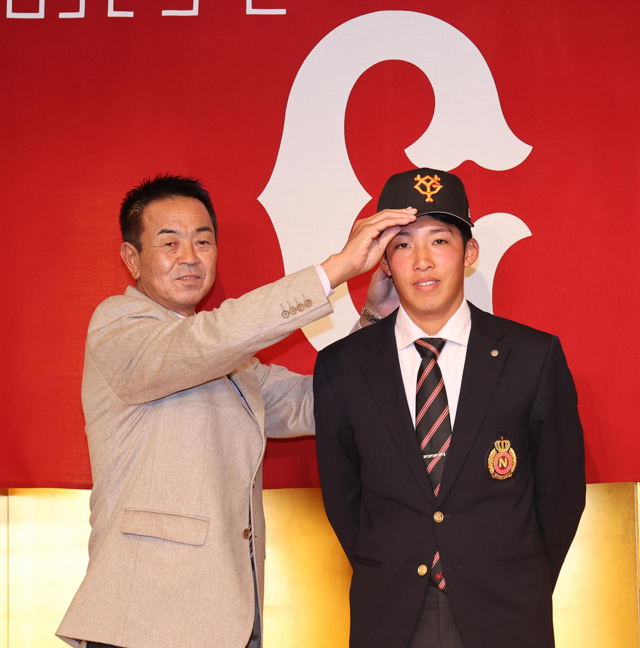 巨人3位指名の日大・赤星（右）は仮契約を終え、巨人水野スカウト部長から帽子をかぶせられる（撮影・野上伸悟）