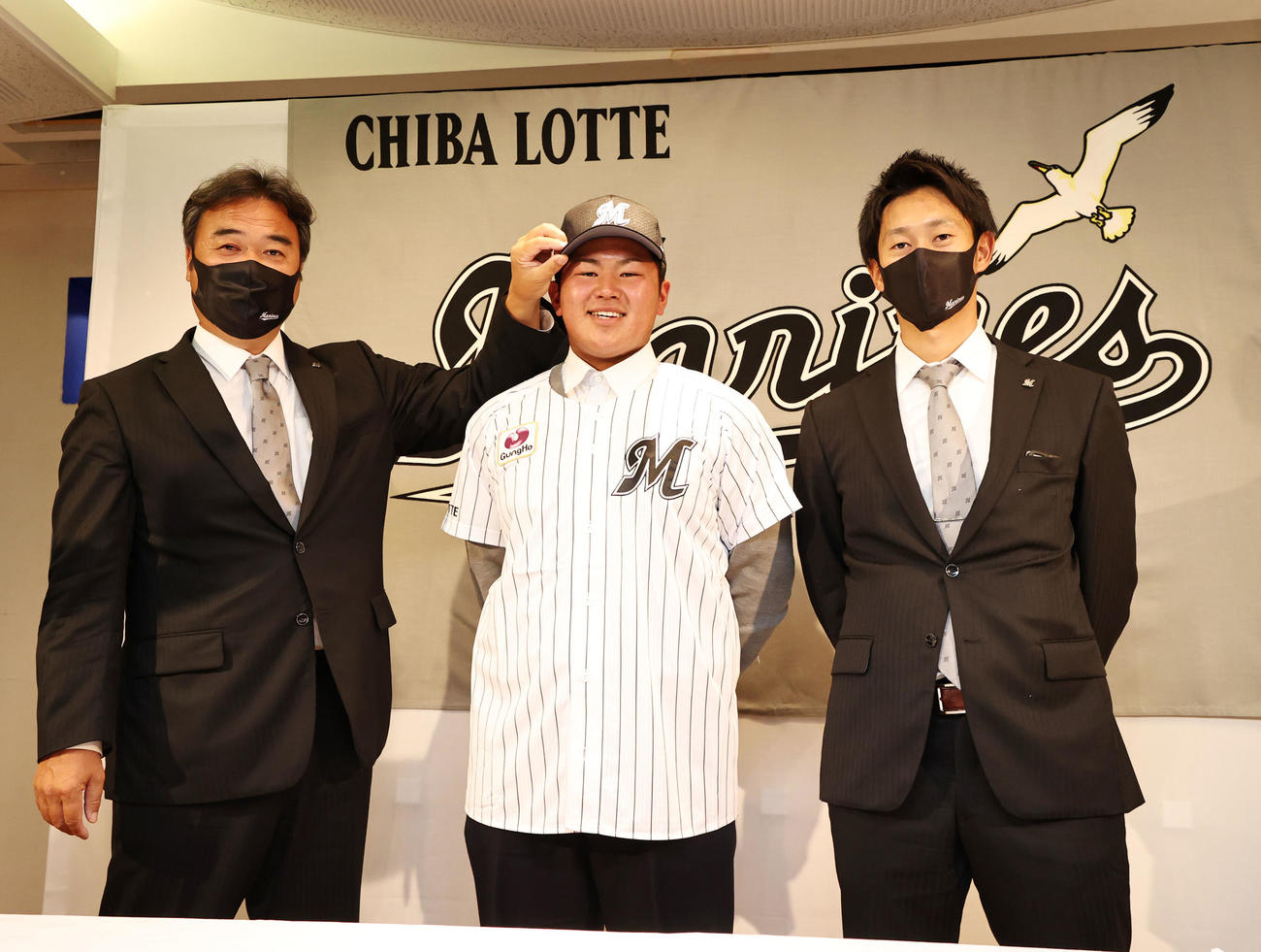 契約交渉を終えたロッテドラフト1巡目指名の松川は永野育成・スカウト部長（左）から帽子をかぶせてもらう。右は三家スカウト（撮影・加藤哉）