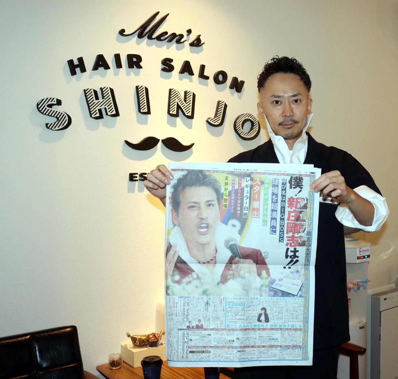 新庄監督就任会見を報じる日刊スポーツを手にしながら、BIGBOSS風に襟を立てる新庄オーナー（撮影・永野高輔）