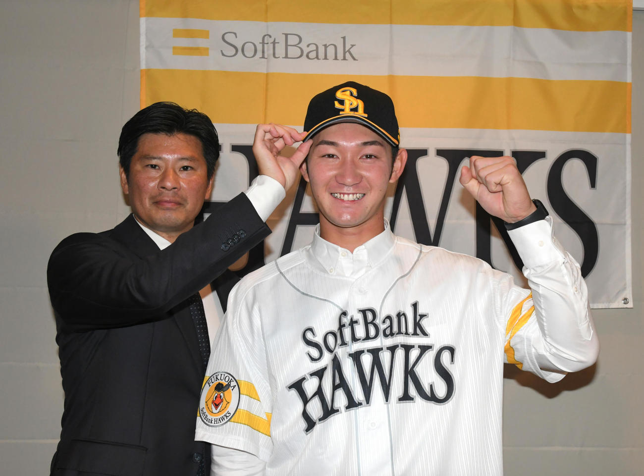 ソフトバンクからドラフト2位指名された慶大の正木智也は、仮契約をすませ山本スカウト（左）から帽子をかぶせてもらう（撮影・酒井清司）