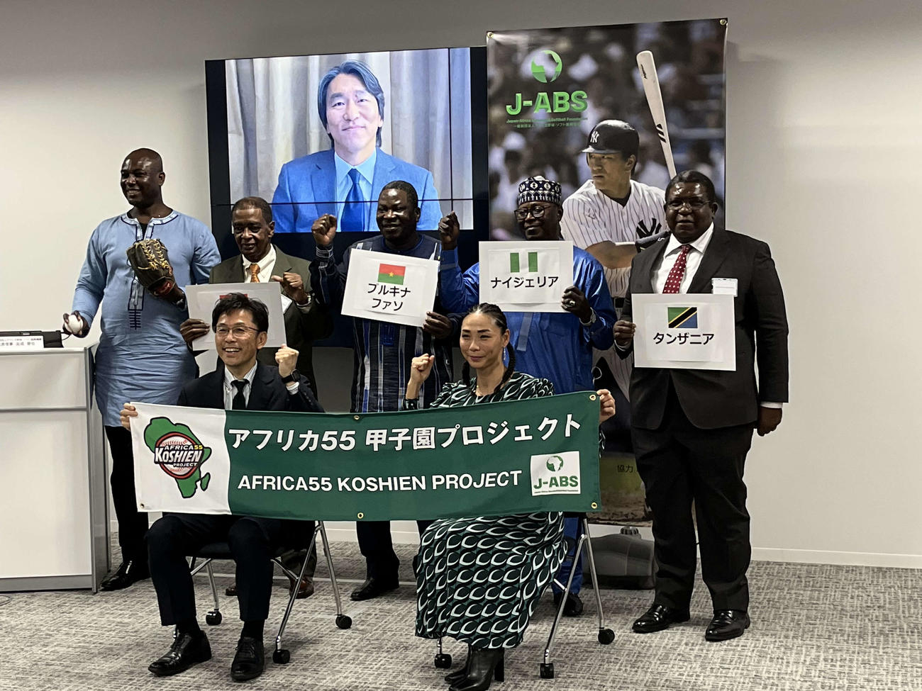 動画メッセージを寄せた松井秀喜氏をバックにアフリカ野球・ソフト振興機構の友成晋也理事（前列左）は各国大使らと記念写真に収まる