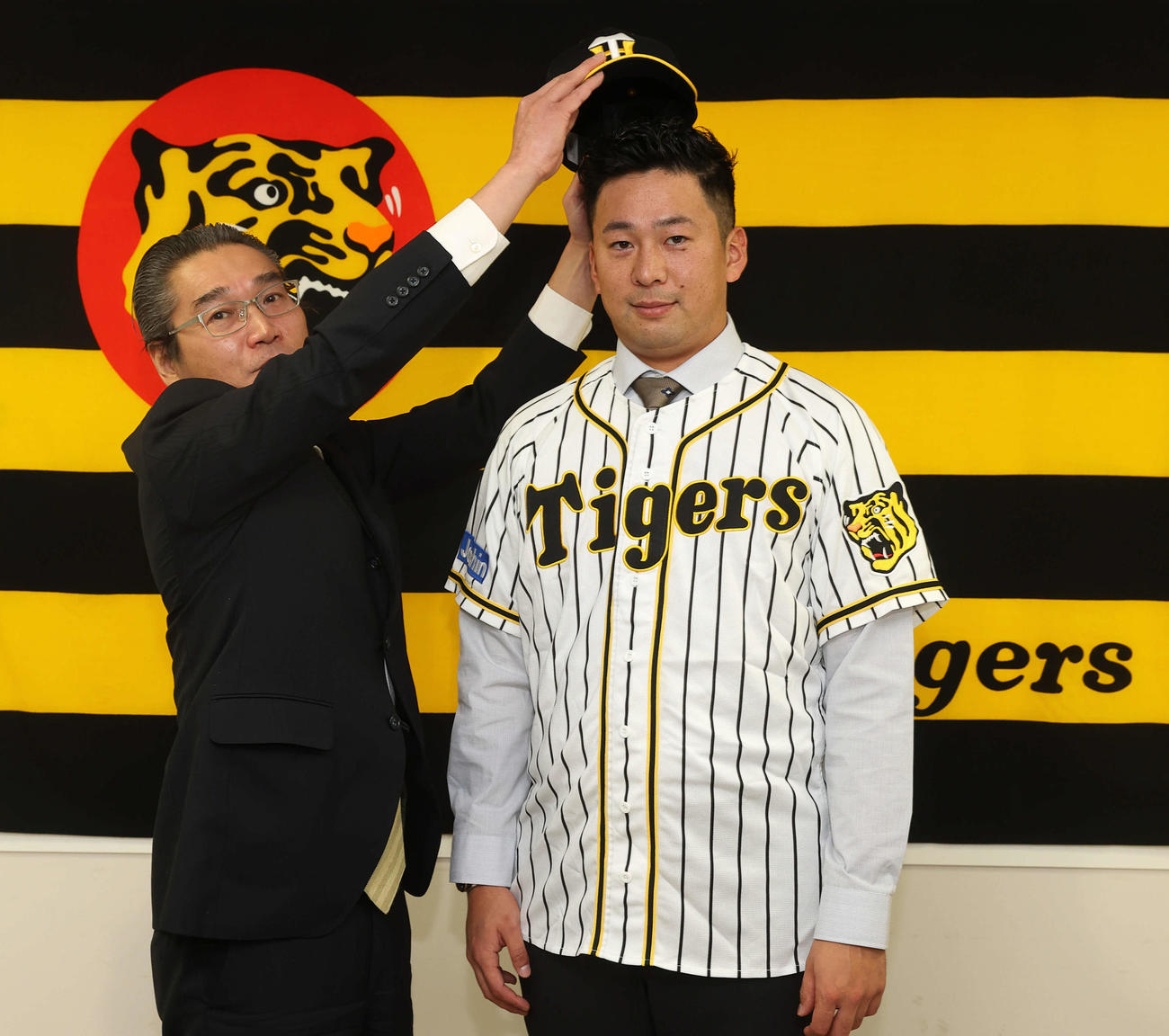 阪神と育成契約を交わした渡辺（右）は嶌村球団本部長から帽子をかぶせてもらう（代表撮影）