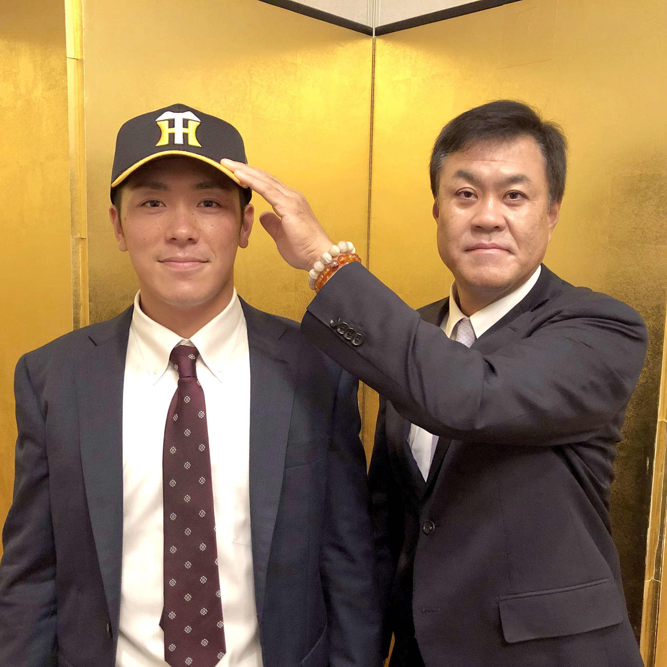 仮契約を終えた阪神豊田（左）は平塚スカウトから帽子をかぶせられ笑顔を見せる（球団提供）