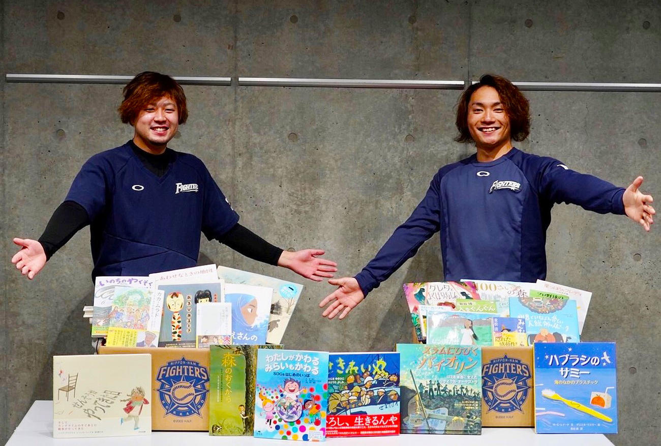ファンから集まった本を前に笑顔を見せる（左から）日本ハム堀瑞輝投手、伊藤（球団提供）