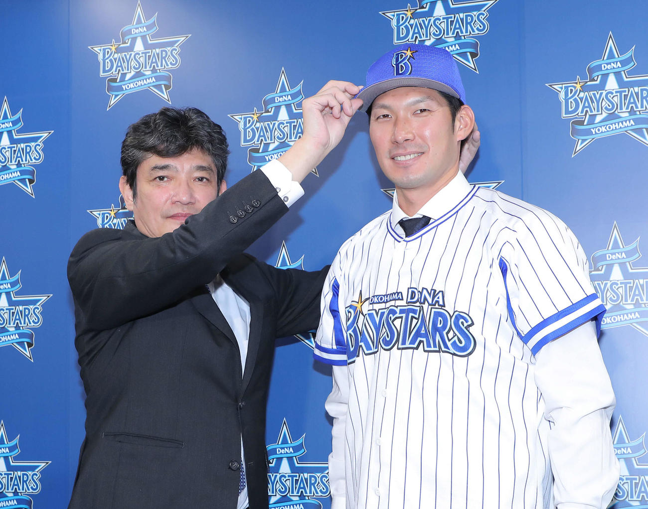 三原球団代表（左）に帽子をかぶせてもらい写真に納まるDeNA大田（撮影・河田真司）