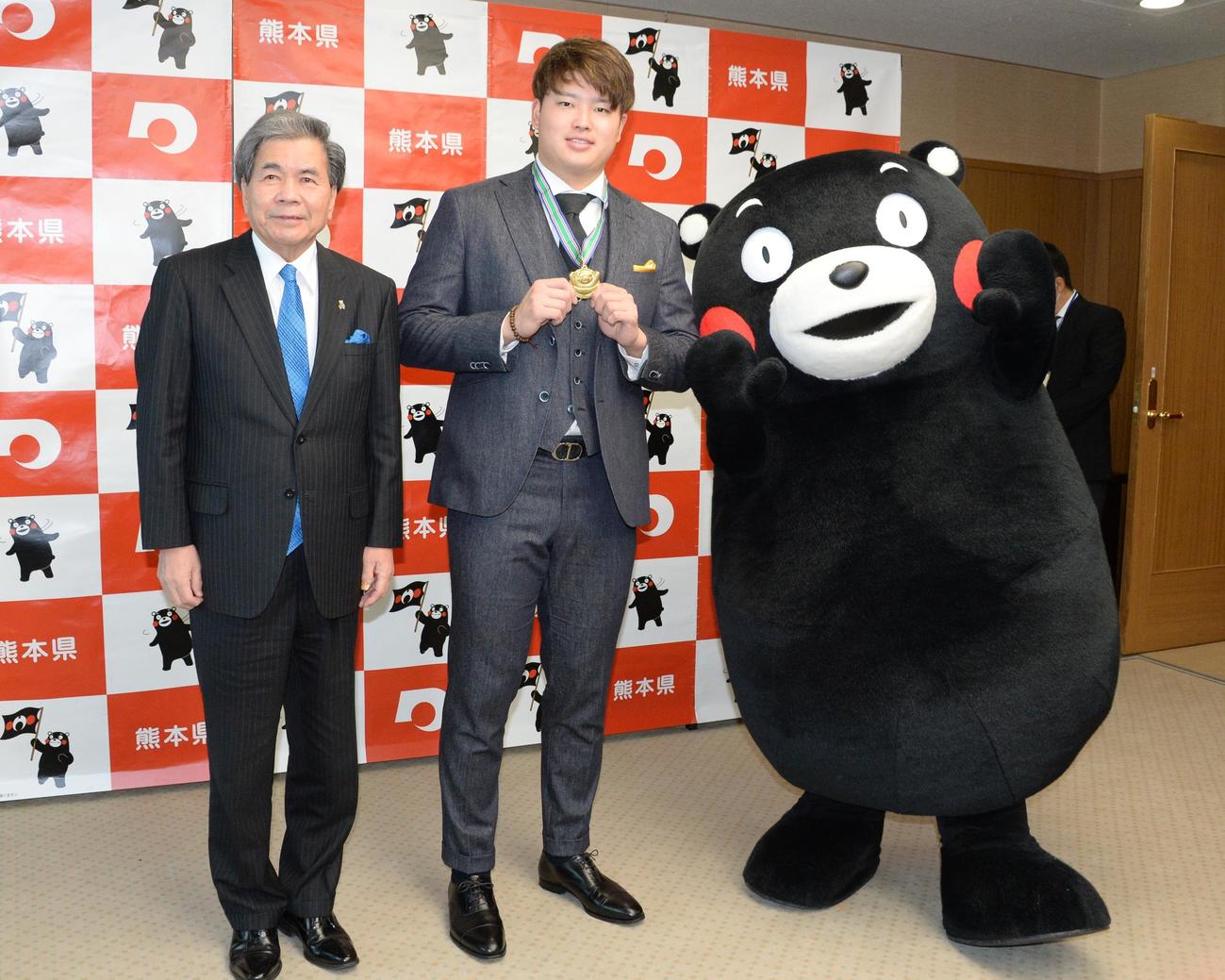 「くまもと夢づくり賞」を受賞したヤクルト村上は、くまもんからの特製の金メダルをかけて笑顔を見せる。左は蒲島知事（撮影・鈴木正章）