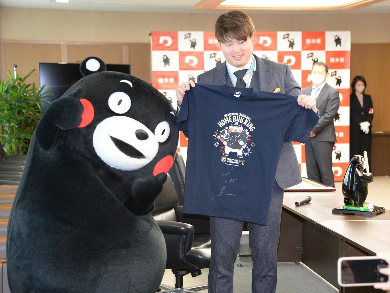 「くまもと夢づくり賞」を受賞したヤクルト村上は、くまモンと自身のコラボTシャツにサインする。右にあるのは副賞のくまモンの置物（撮影・鈴木正章）