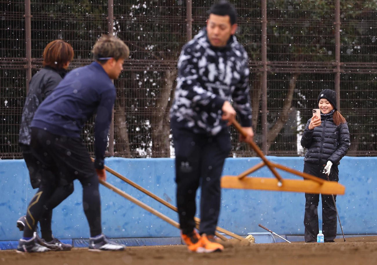 合同自主トレでノックを終えグラウンド整備する選手たちを撮影する三ヶ島（右）（撮影・垰建太）