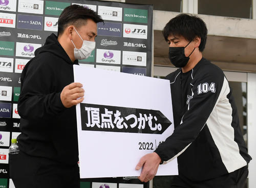 22年1月31日、井口監督の会見でスローガンのボードを渡す手嶌広報兼打撃投手（右）