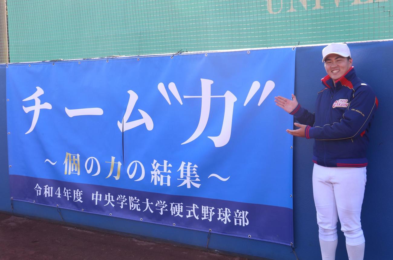 新チームのテーマ「チーム力～個の力の結集～」の横断幕を笑顔で紹介する、中央学院大・塩塚陽人主将（撮影・阿部泰斉）