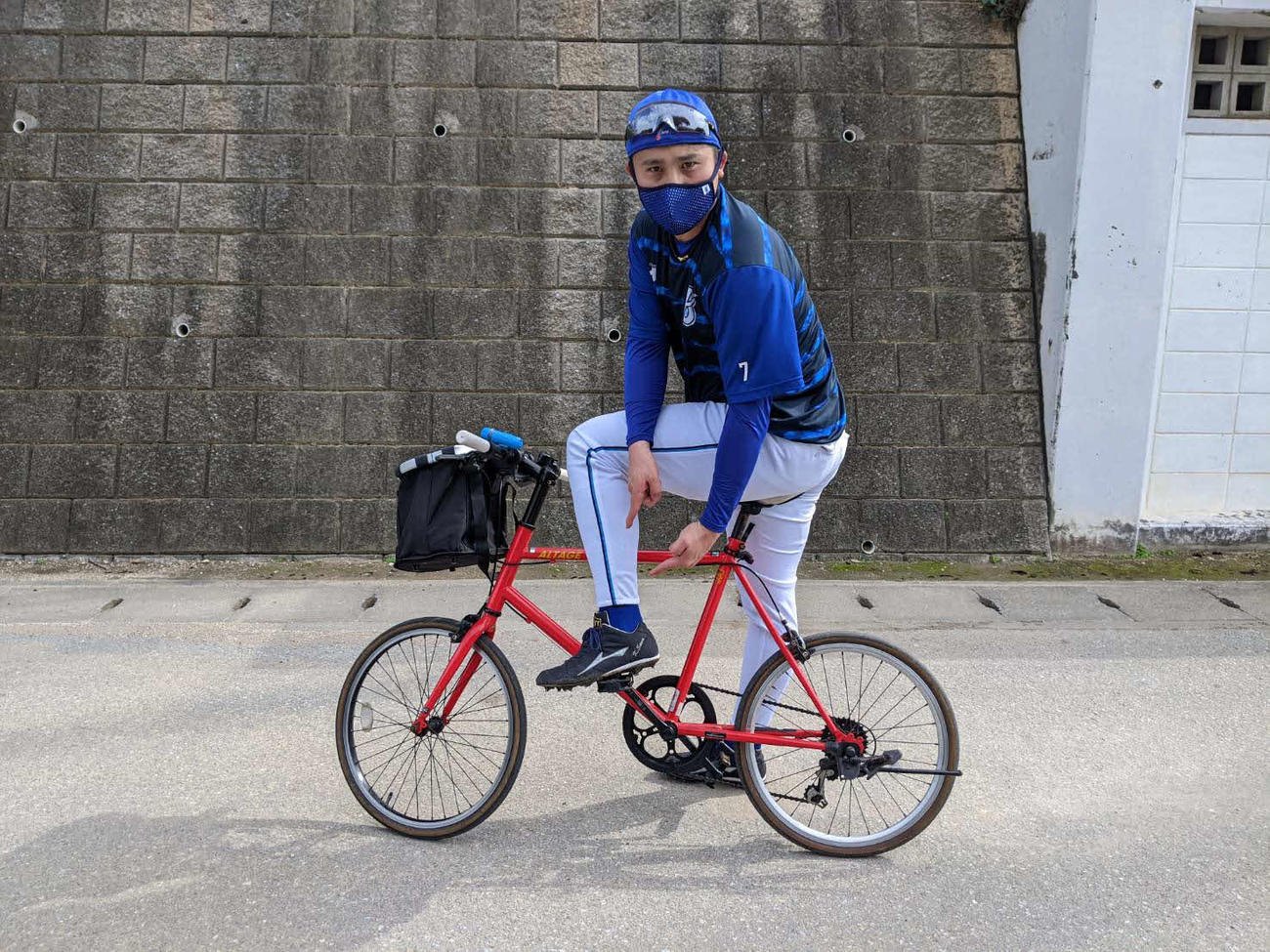 自転車に乗りながら、パドレス・タティスのようにユニホームの裾を絞ったズボンを指さすDeNA佐野（球団提供）