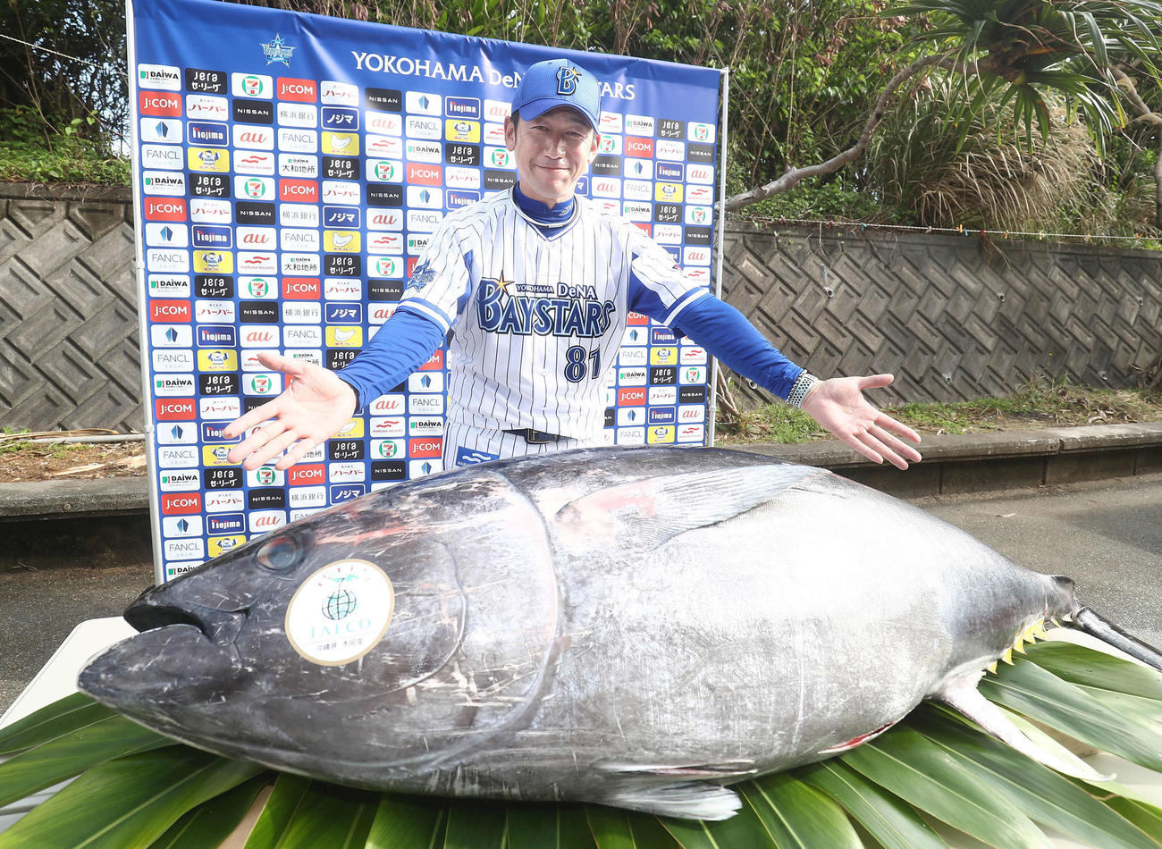 マルハニチログループで養殖されたクロマグロを前に、両手を広げ笑顔を見せるDeNA三浦監督