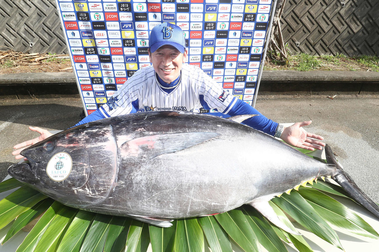 マルハニチログループで養殖されたクロマグロを前に、両手を拡げ笑顔を見せるDeNA三浦監督