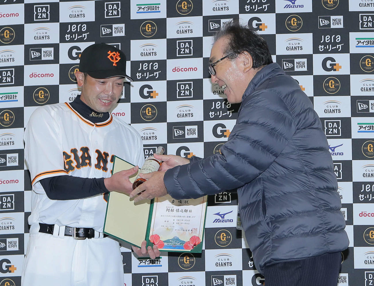 伊江村観光親善大使委嘱状交付式で伊江村長の島袋氏（右）から特産品のラム酒を受け取る阿部作戦兼ディフェンスチーフコーチ（撮影・河田真司）