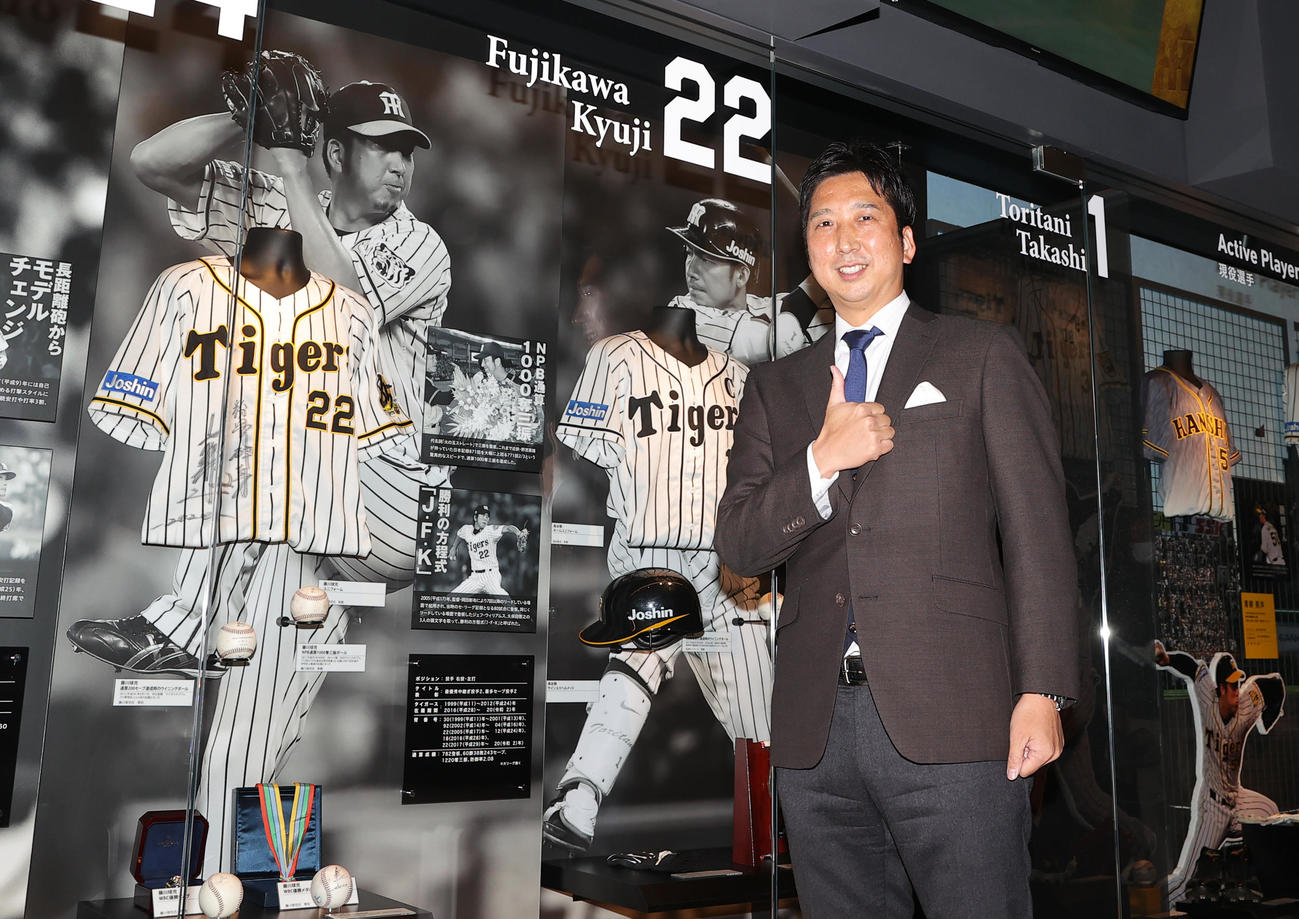 リニューアルした甲子園歴史館に展示されるユニホームを横にポーズを決める阪神藤川SA（撮影・上山淳一）