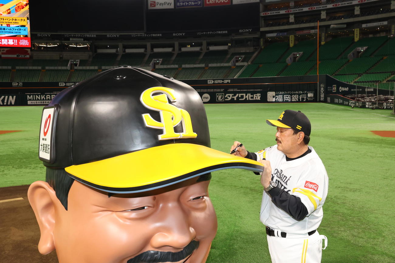 「BIG FACE藤本」の巨大な帽子にサインするソフトバンク藤本監督（球団提供）