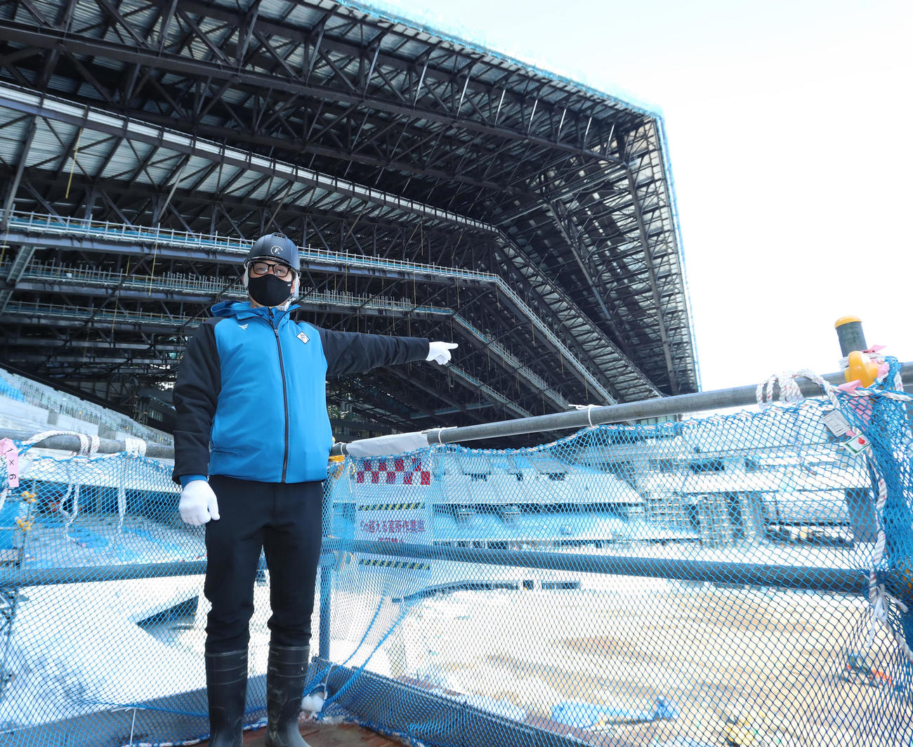 日本ハム新球場のエスコンフィール北海道を背に指をさす株式会社ファイターズスポーツ＆エンターテイメント取締役事業統轄前沢本部長（撮影・佐藤翔太）