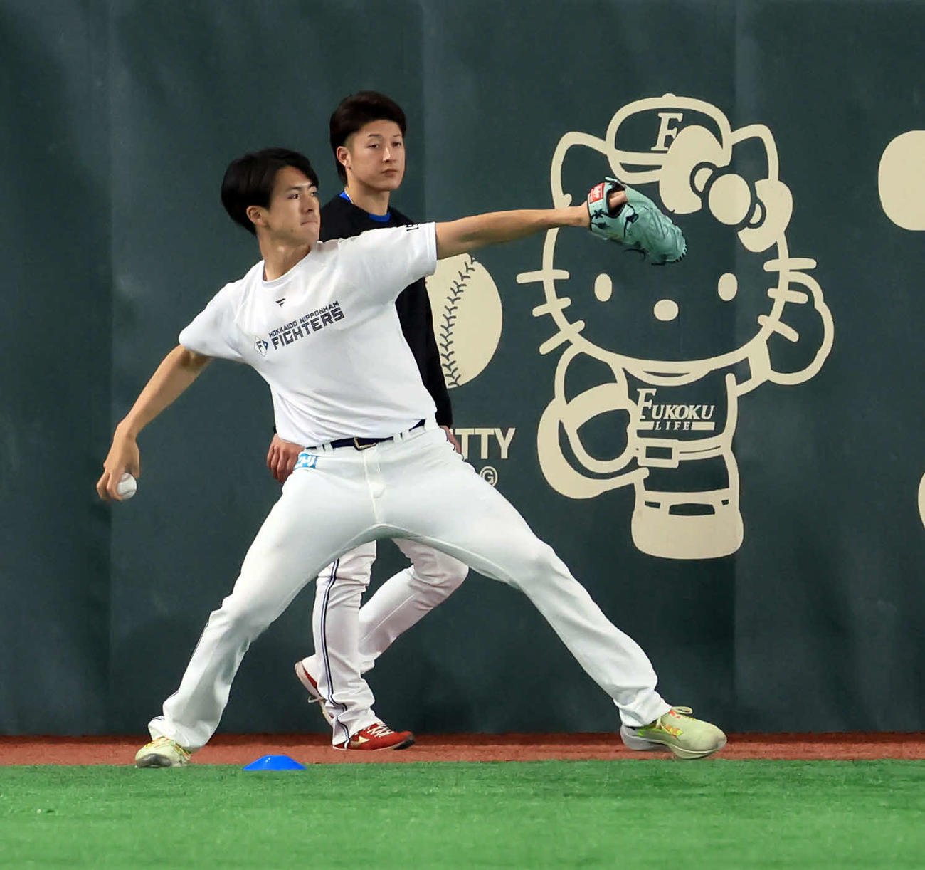 日本ハム対オリックス　試合前練習でキティちゃんの看板を背にキャッチボールする日本ハム上沢（左）。奥は吉田（撮影・浅見桂子）