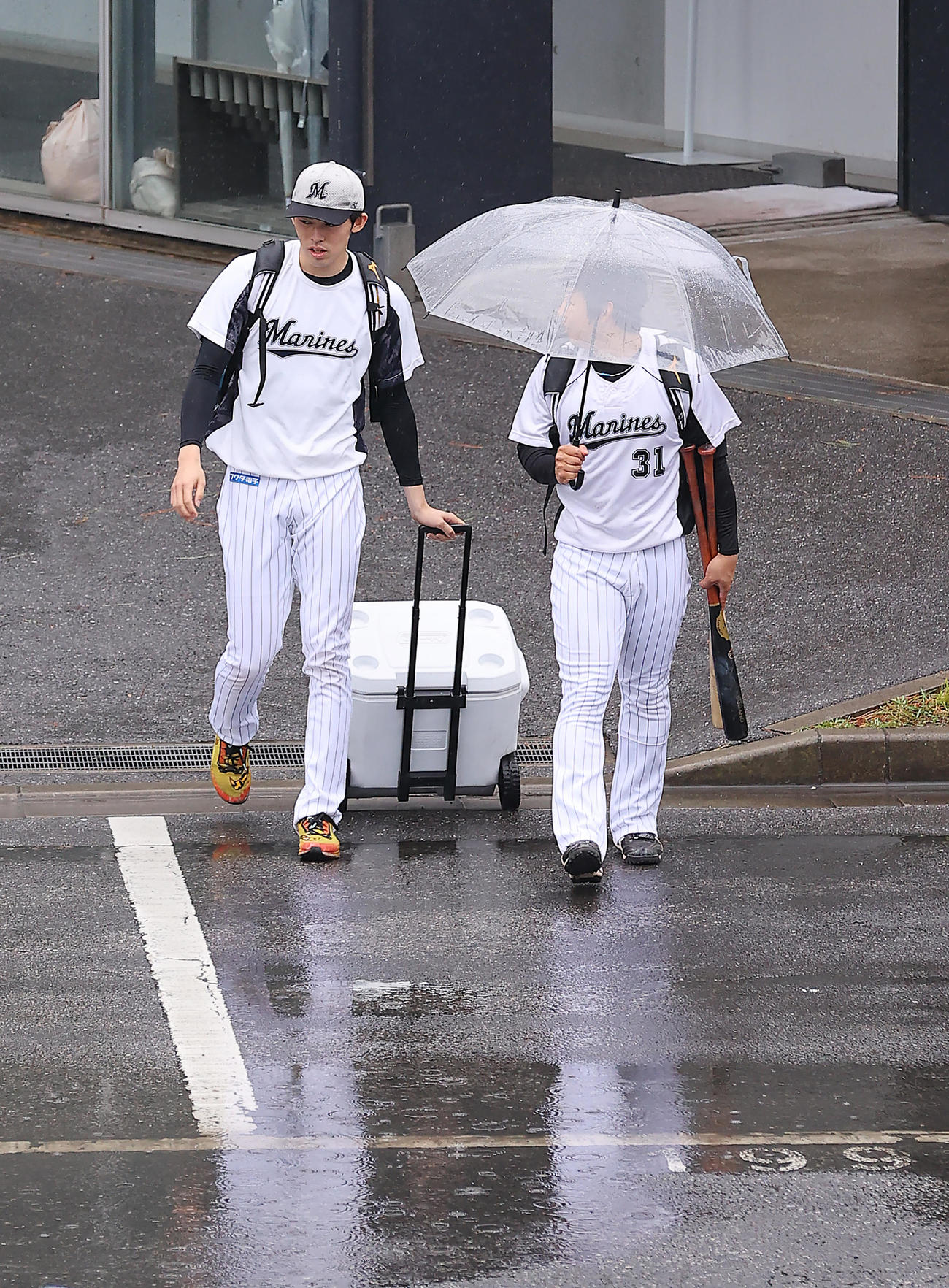 ロッテ対日本ハム　雨天中止となり、水たまりを避けながら室内練習場を後にするロッテ佐々木朗（左）、菅野（撮影・垰建太）