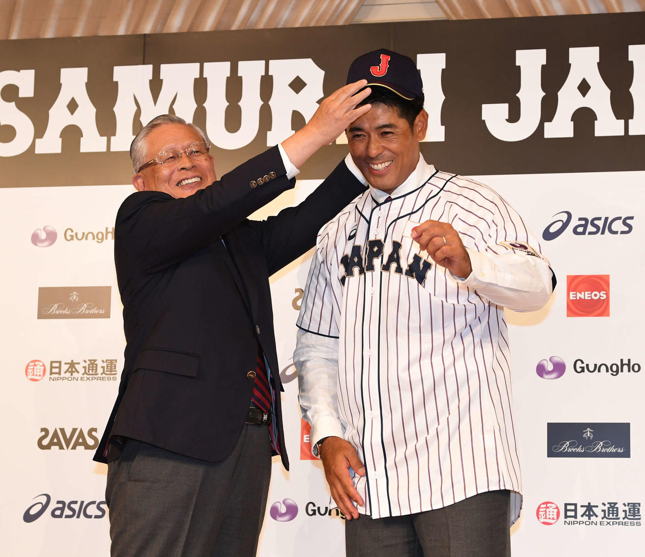 日本野球協議会の熊崎会長（左）に帽子をかぶせてもらい笑顔を見せる侍ジャパン稲葉監督（2017年7月31日撮影）