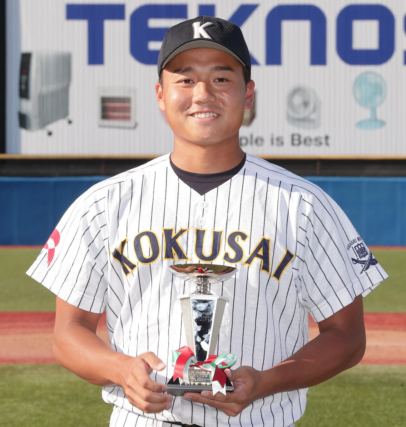 首位打者賞を受賞し、トロフィーを手に笑顔を見せる東日本国際大・上崎（撮影・野上伸悟）