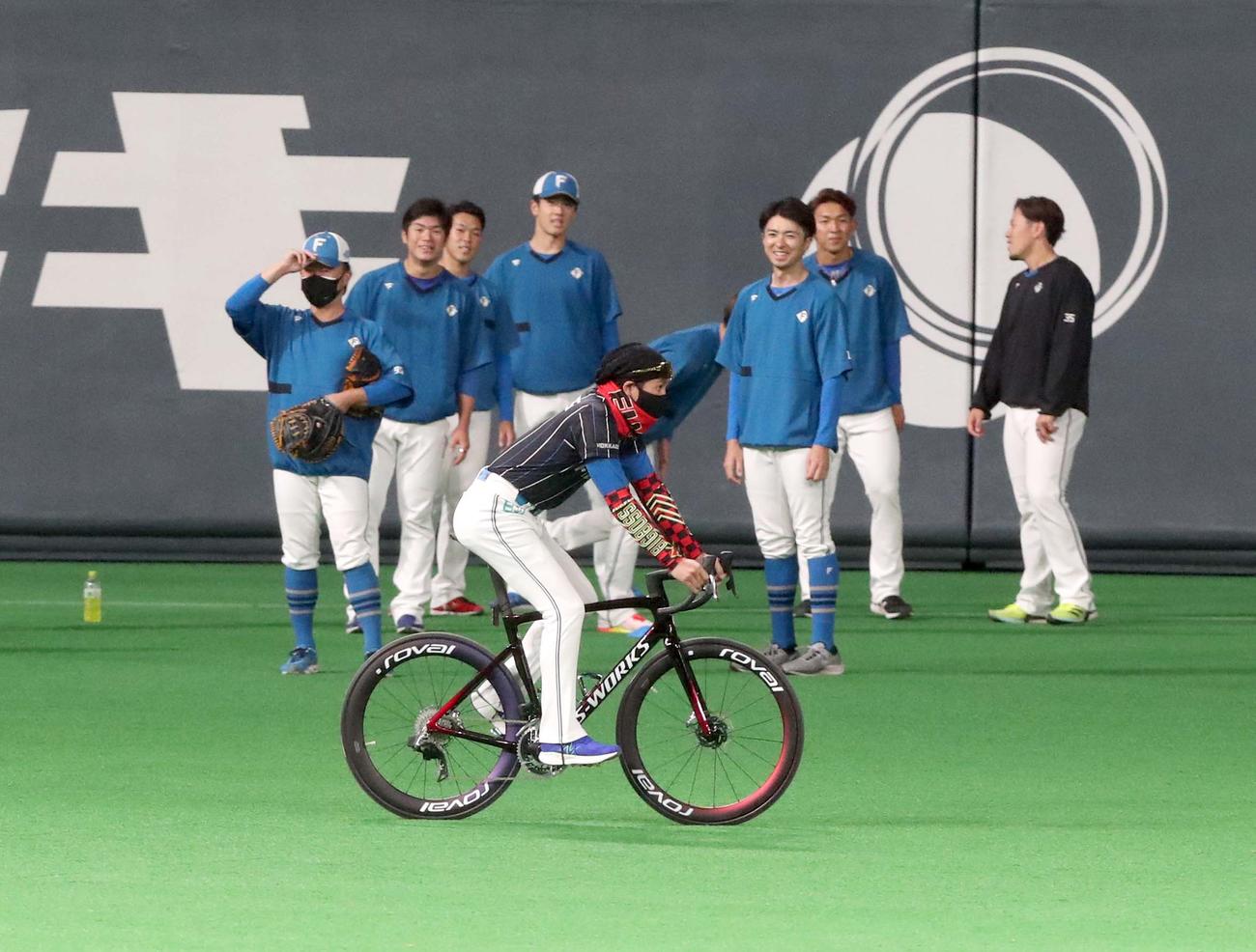 グラウンドをロードバイクで走る日本ハム新庄監督。練習中の選手も興味深げに見つめる（撮影・黒川智章）