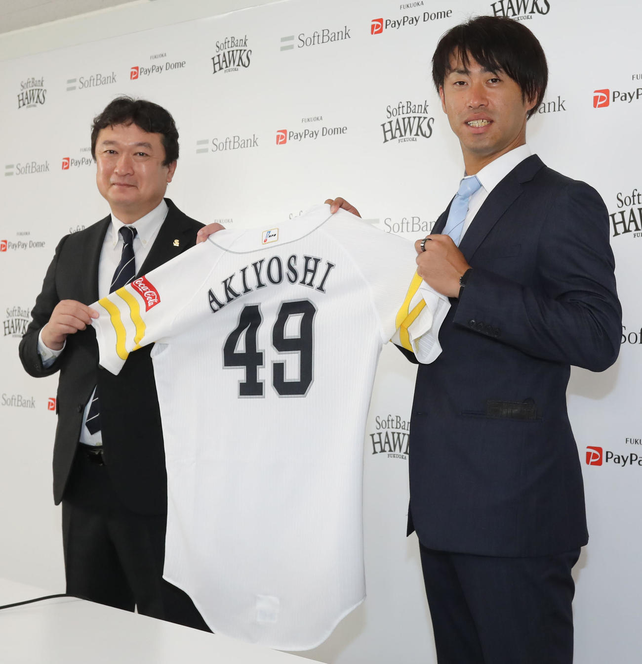 入団会見で背番号49番のユニホームを披露する三笠取締役GM（左）と秋吉（撮影・屋方直哉）