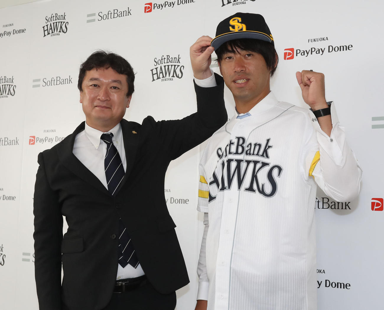 入団会見でユニホームに袖を通す秋吉。左は三笠取締役GM（撮影・屋方直哉）