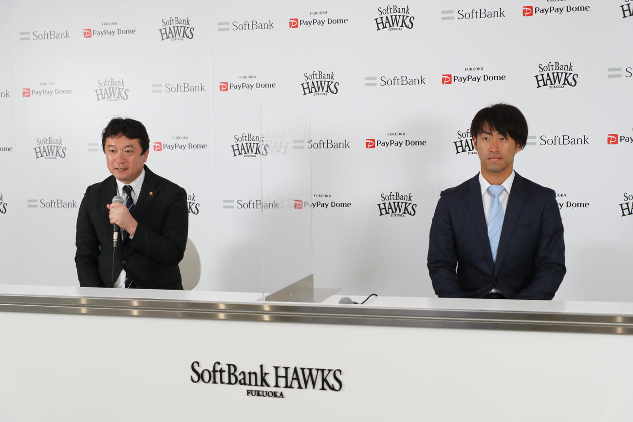 入団会見で三笠取締役GM（左）の話を聞く秋吉亮投手（外部提供）