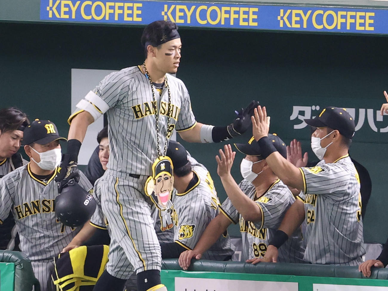 巨人対阪神　3回表阪神2死一塁、2点本塁打を放ち、矢野監督のイラストが描かれた飾りをかけ、チームメートに迎えられる佐藤輝（撮影・狩俣裕三）