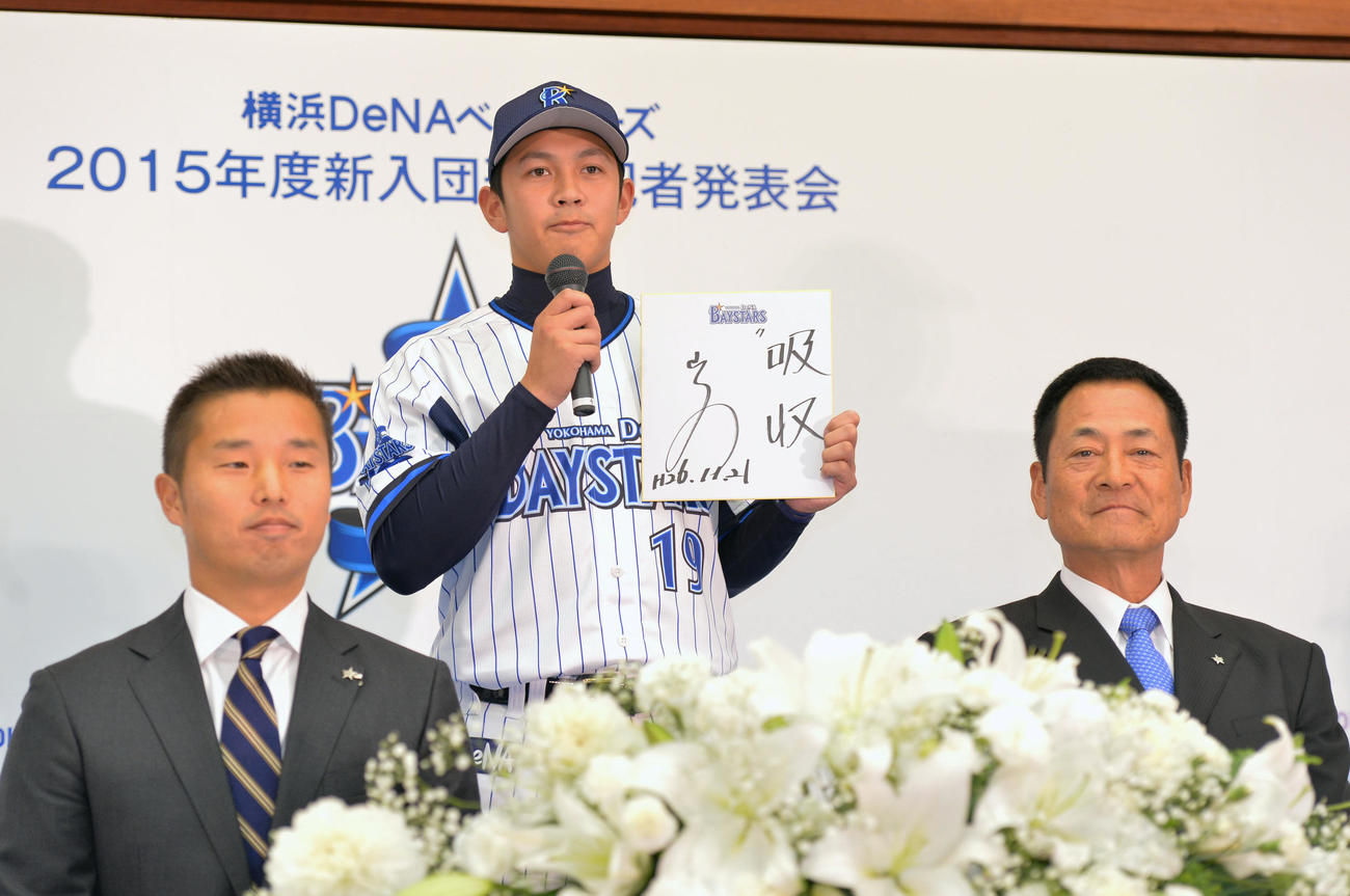 2014年11月21日、新入団選手発表会で山崎康（中央）はプロへ入ってからの目標「吸収」を披露する。左は池田球団社長、右は中畑監督