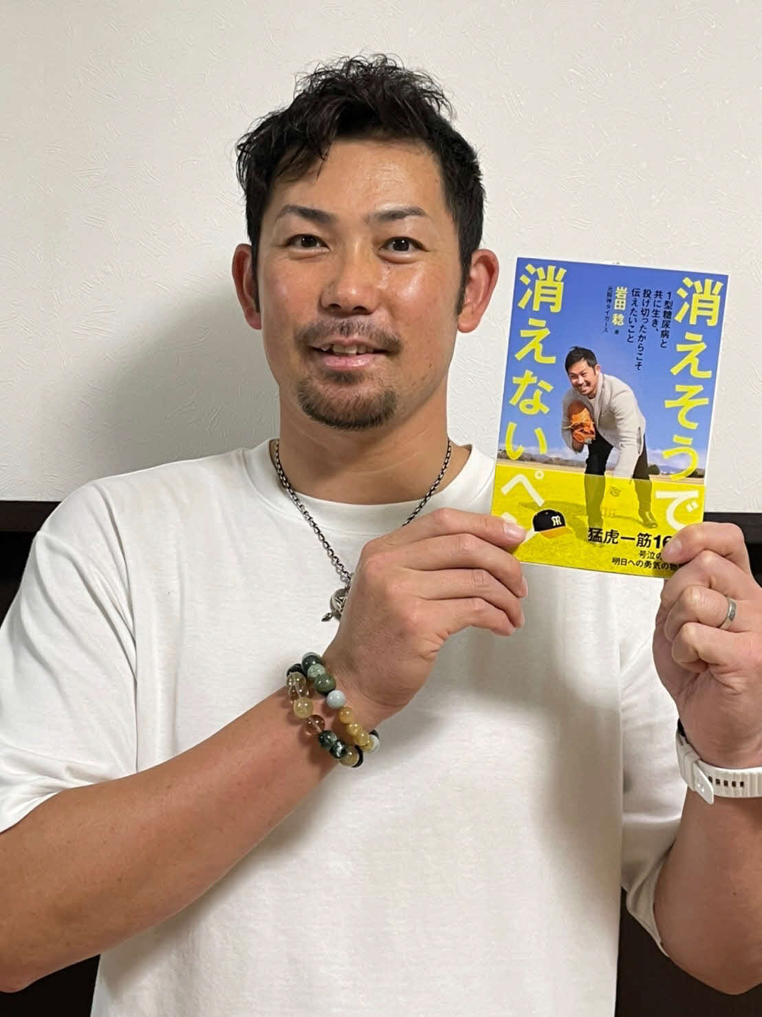 阪神CAで日刊スポーツ評論家の岩田稔氏は著書「消えそうで消えないペン」を手に笑顔（本人提供）