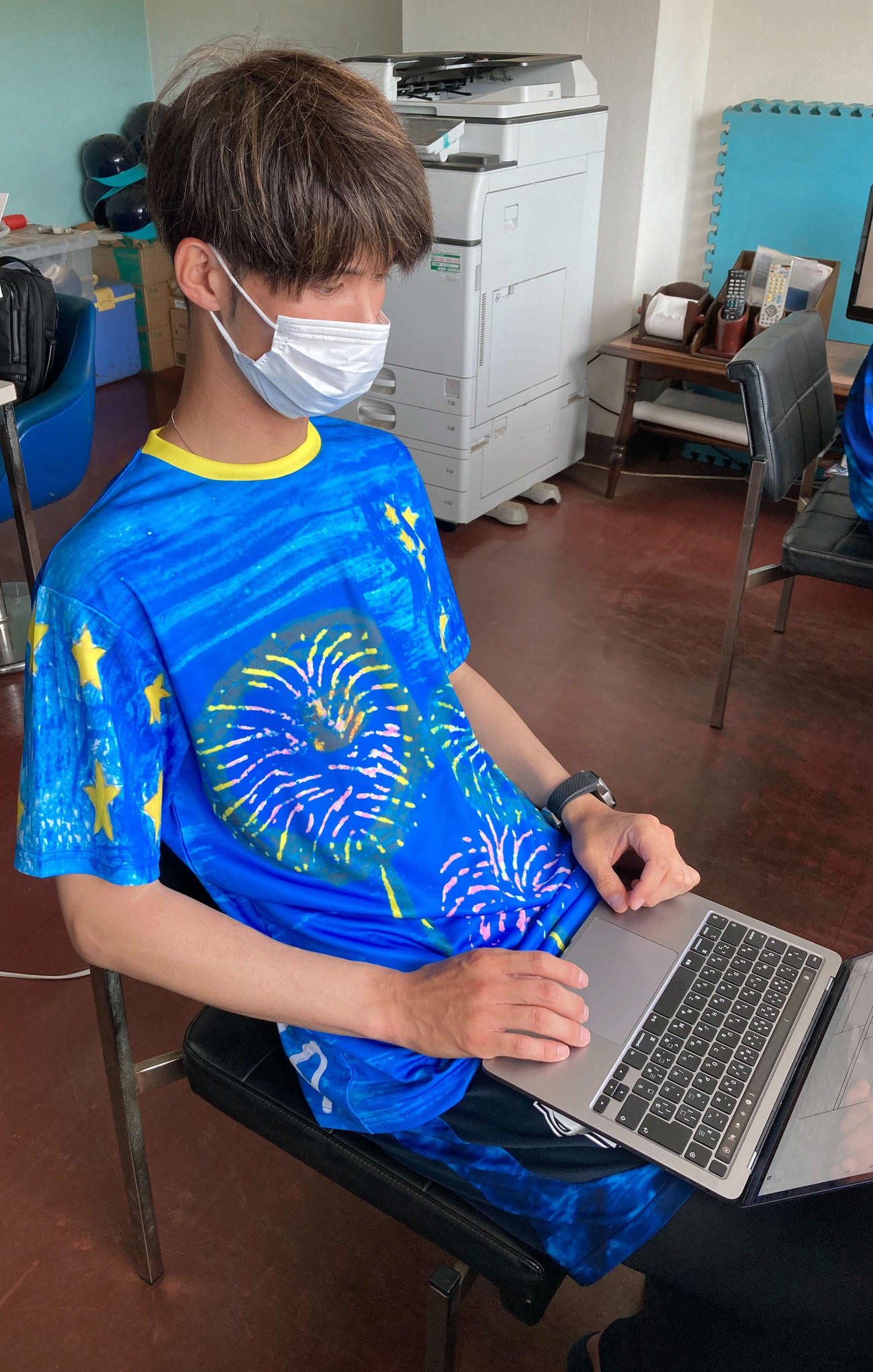 小学5年生の女の子がデザインしたチームウエアを着用し、パソコンで作業するDeNA小杉ファーム投手コーチ（球団提供）