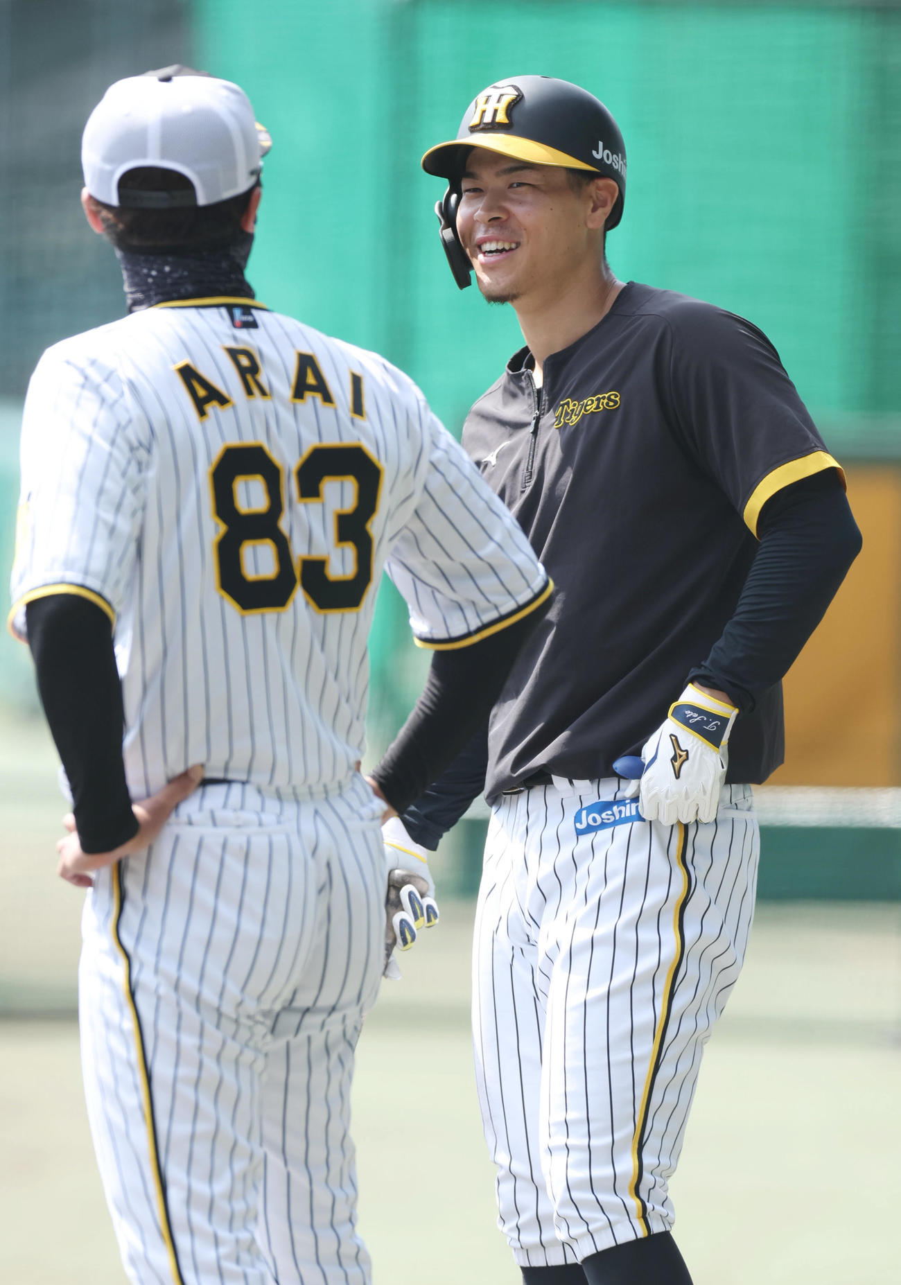 練習中、阪神新井コーチ（左）と談笑する佐藤輝（撮影・前田充）