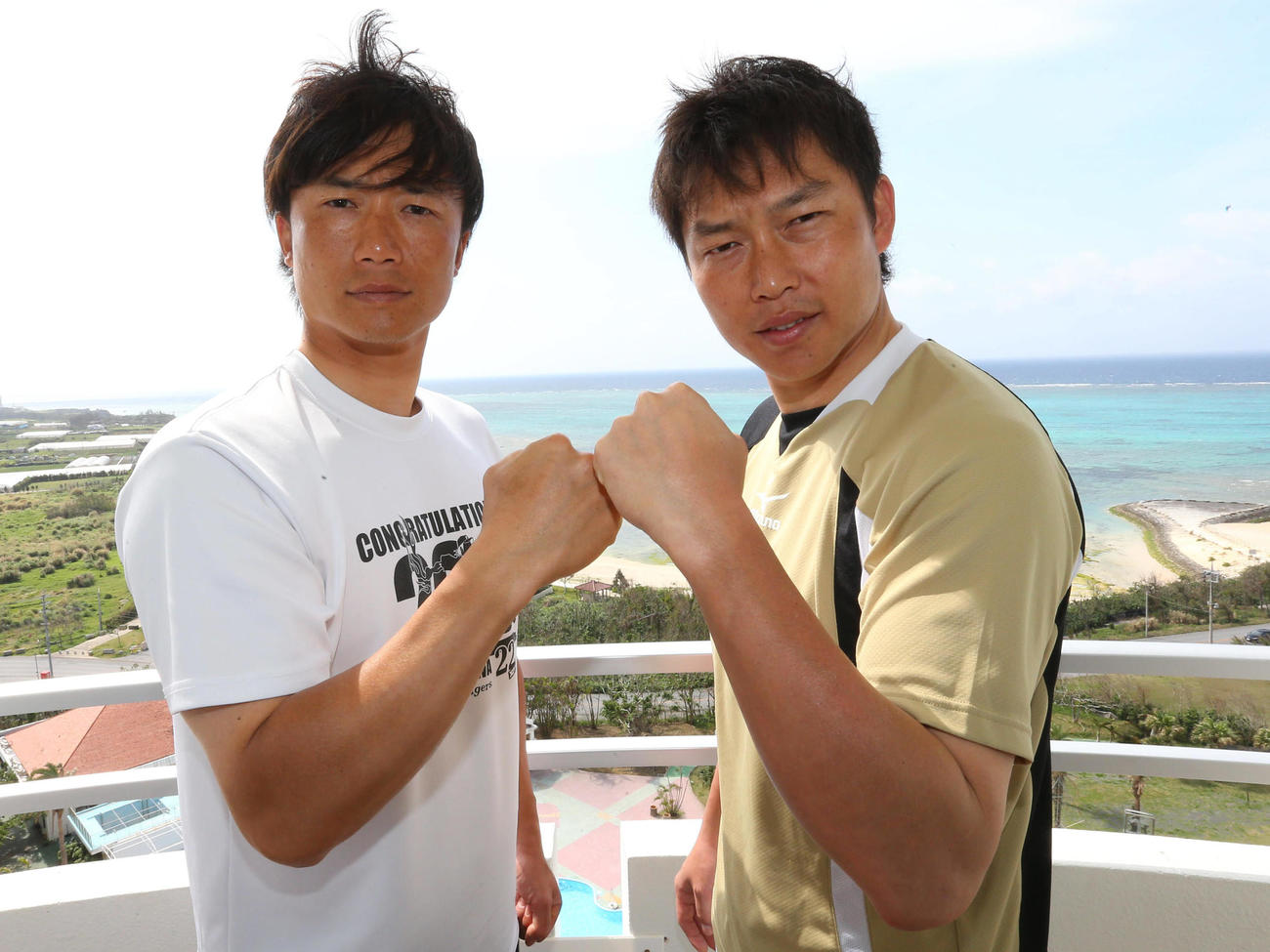 2013年2月12日、沖縄の海をバックに拳を合わせる新井貴（右）と新井良