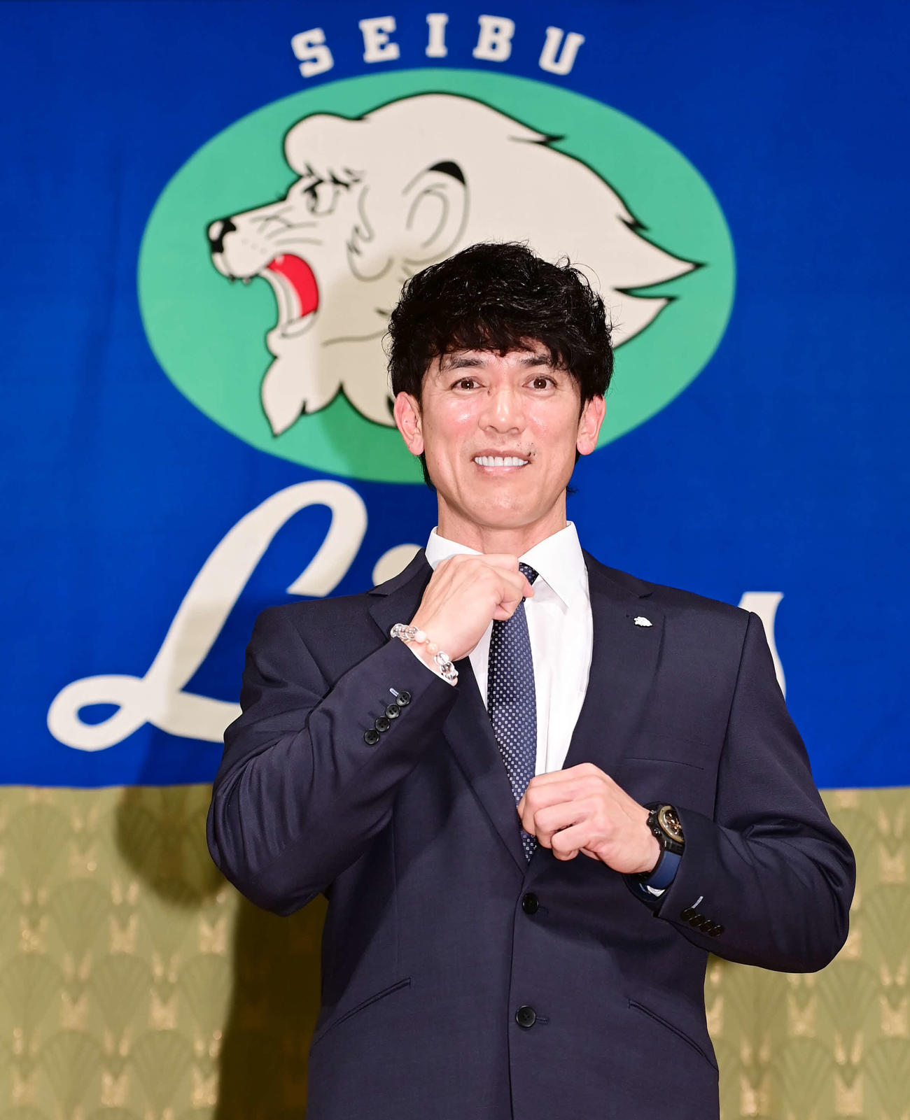 就任会見でライオンズブルーを意識して着用した青いネクタイを手に笑顔を見せる西武松井新監督（撮影・小沢裕）　