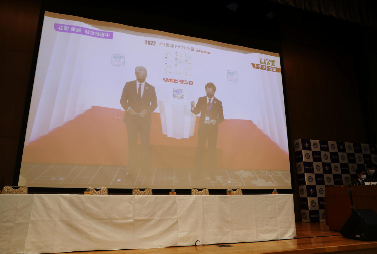 選手ら不在の立大の会場で放送される荘司の指名1位獲得交渉権を獲得する楽天の米田球団社長（右）の様子。左はロッテ吉井新監督（撮影・狩俣裕三）