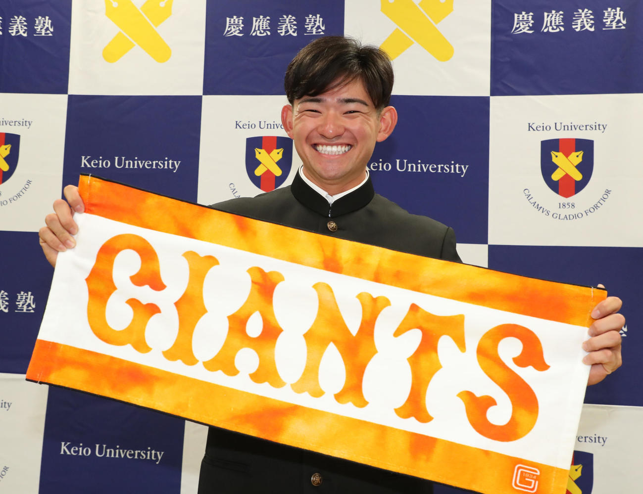巨人から指名を受け応援タオルを手に笑顔の慶大・萩尾（代表撮影）