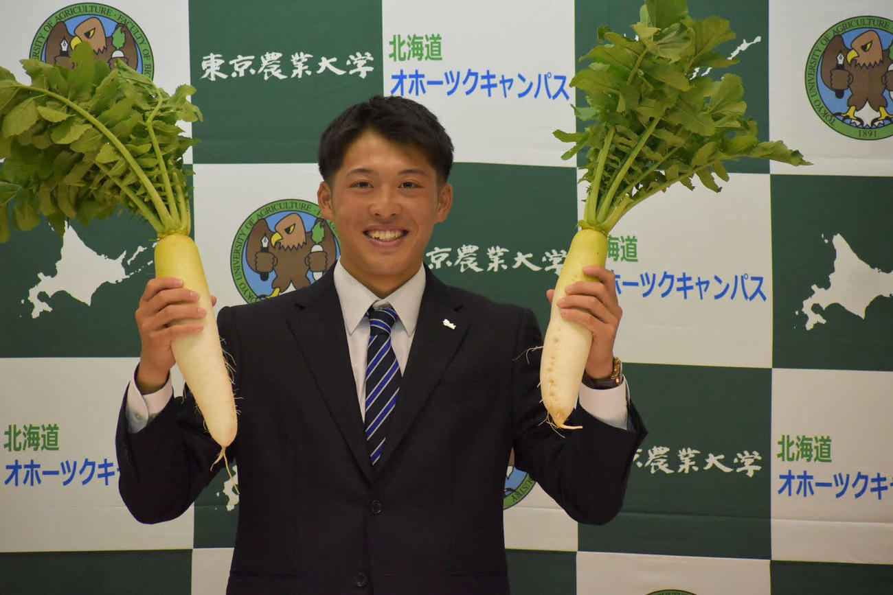 楽天から4位で指名された東農大北海道オホーツク・伊藤は大根を手に笑顔を見せる（同校提供）