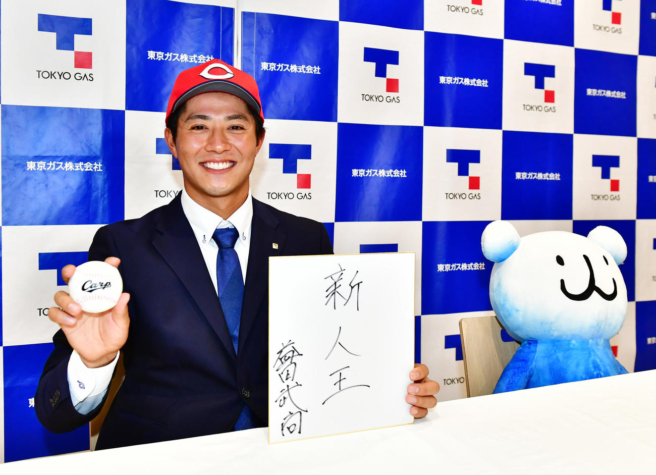 広島から3位指名を受けた東京ガス・益田武尚はプロでの目標を新人王と色紙に認める。右はマスコットのパッチョ（撮影・小沢裕）　