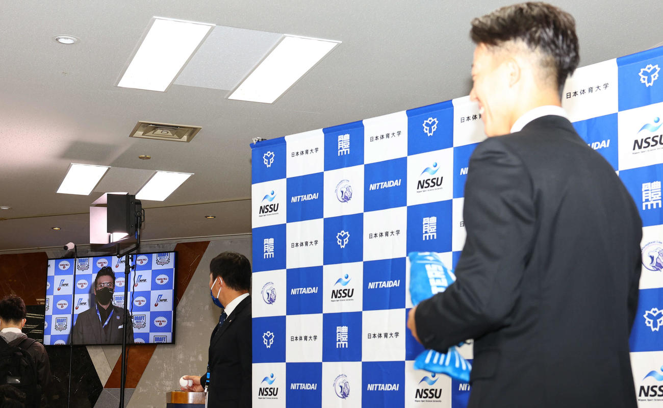 日本ハムから1位指名を受けた日体大・矢沢（右）は中継の新庄監督の言葉に笑顔を見せる（撮影・垰建太）